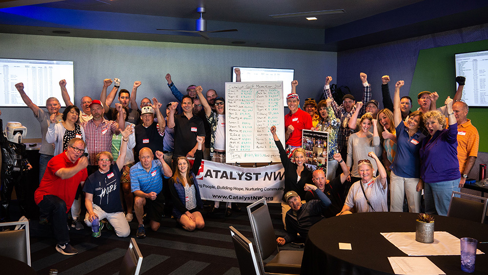 Group of people fist pumping in the air with a tally of funds raised, and the sign Catalyst NW