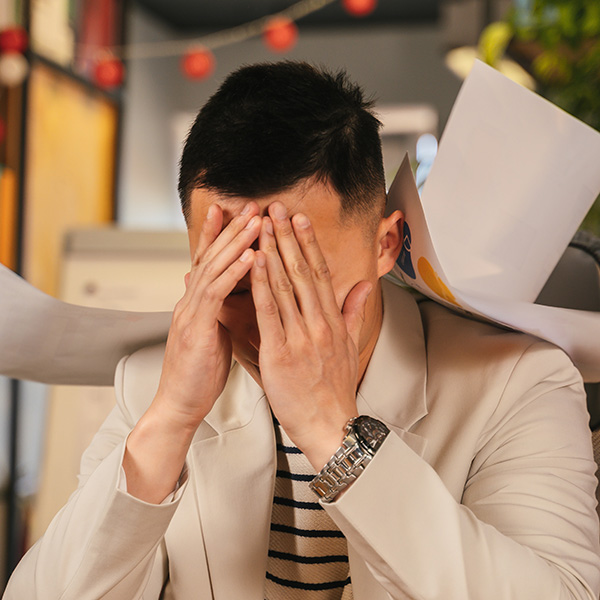 Asian man frustrated at work with papers falling around him